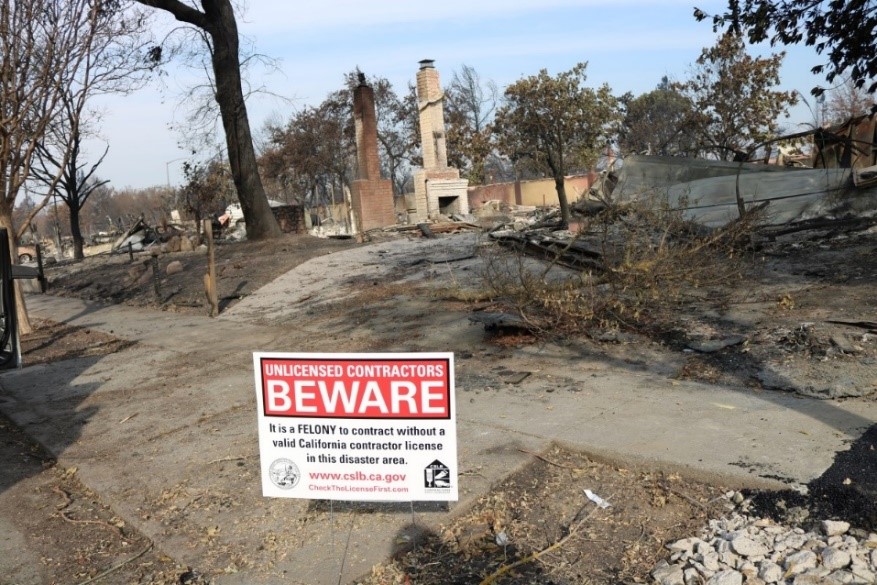 photo of a disaster signe warning unlicensed contrators to avoid working in a disaster area with fire debris in the background